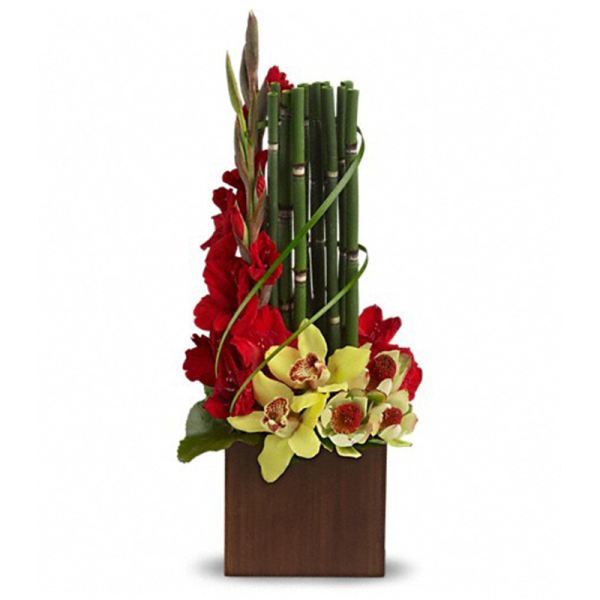 Tall modern arrangement with red snapdragons, green bamboo stalks, and yellow orchids in a wooden cube vase