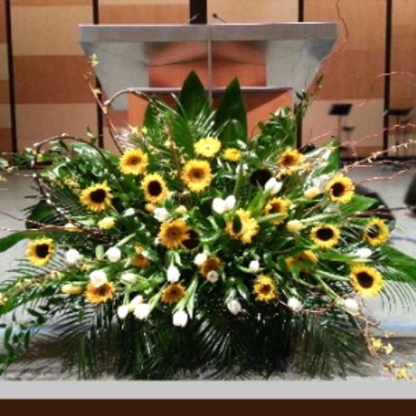 Large stage arrangement of yellow sunflowers and white tulips in an asymmetrical spray.