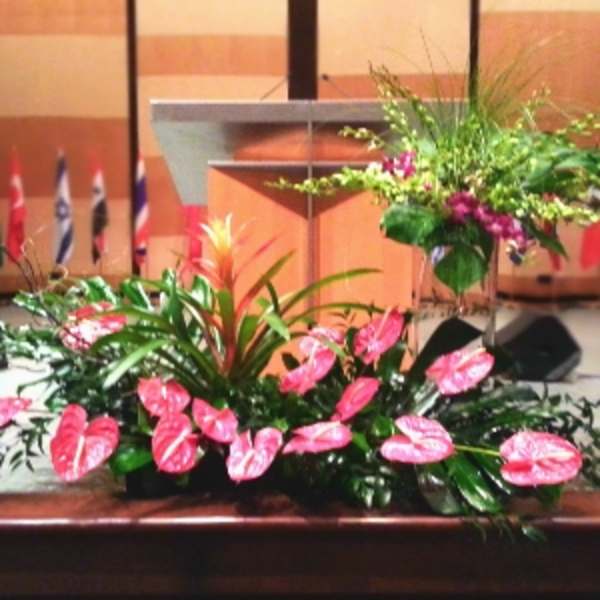 Stage floral display with pink tropical flowers and an orange accent plant before a podium
