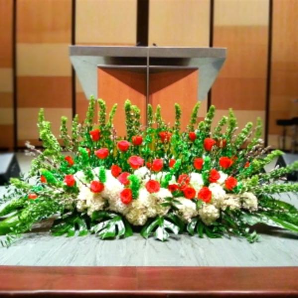 Large altar spray with red roses, white hydrangeas, and tall green spikes in front of a podium