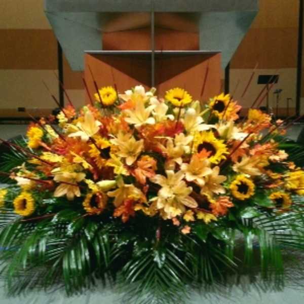 Large low altar-style arrangement of yellow lilies and sunflowers with orange blooms and palm fronds