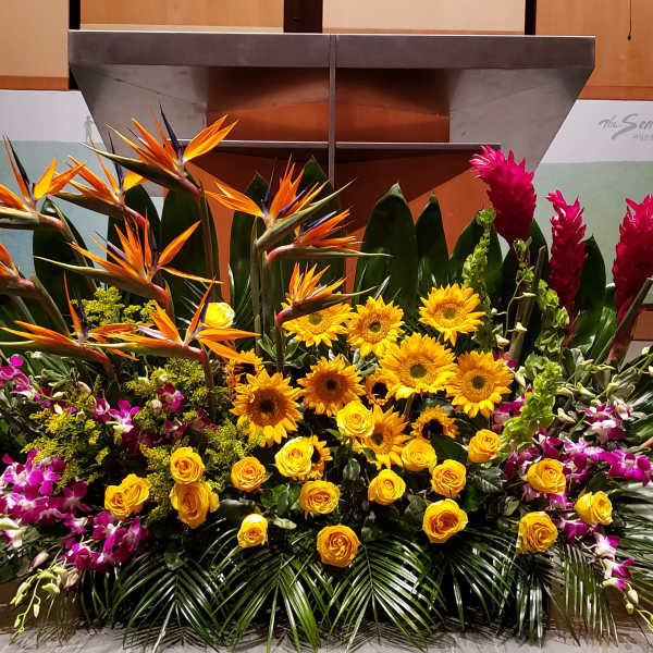 Large tropical stage arrangement with yellow sunflowers, roses, birds of paradise, orchids, and red ginger