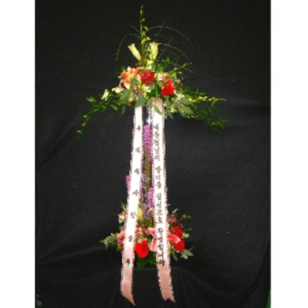 Tall two-tiered standing floral spray with red flowers and printed ribbons on a black background