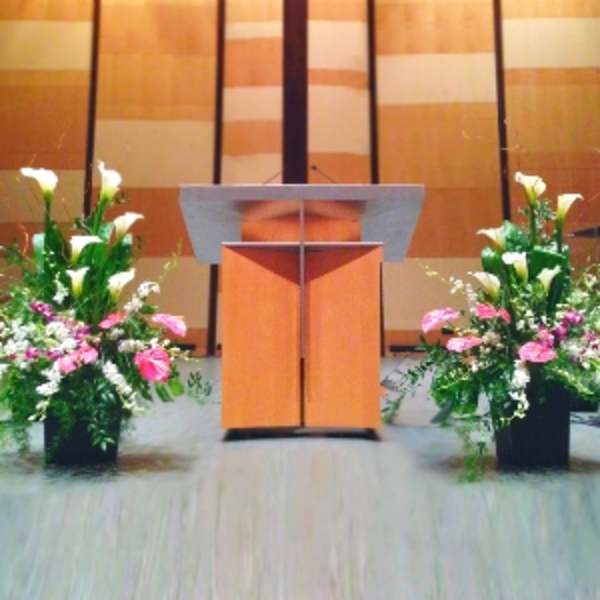 Two large floral arrangements with white calla lilies and pink flowers flanking a wooden podium.