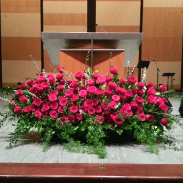 Large low arrangement of bright pink roses with white accent flowers in front of a podium