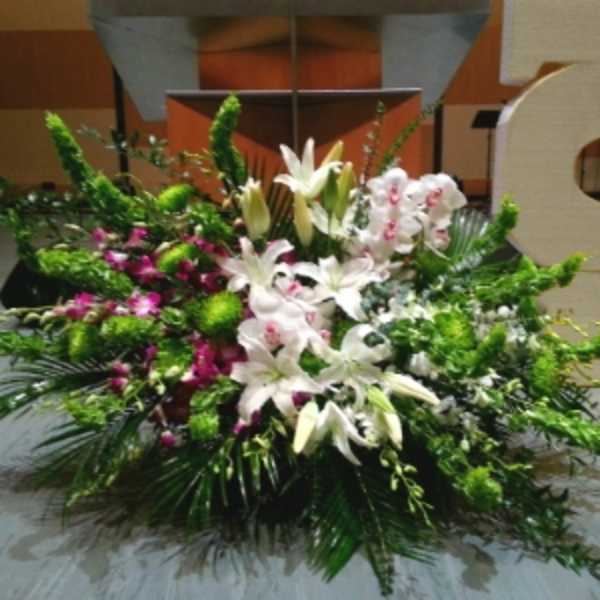 Large white lily and orchid floor arrangement with green accents in front of a stage