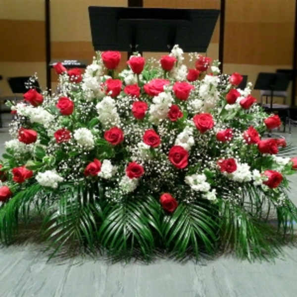 Large fan-shaped arrangement of red roses and white flowers with palm fronds on a stage.