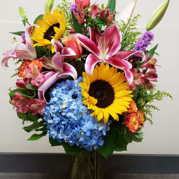 Mixed bouquet with sunflowers, lilies, hydrangeas, and roses in a glass vase