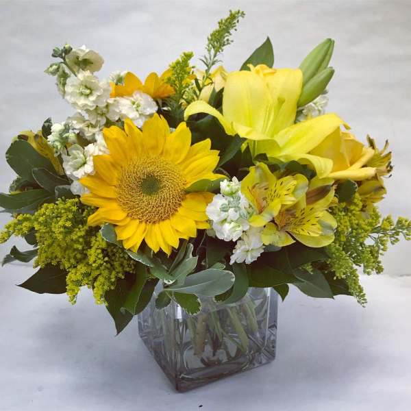 Yellow flowers arranged in a clear square glass vase