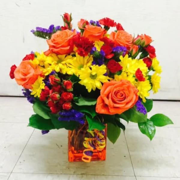 Colorful bouquet of roses and daisies in a square glass vase