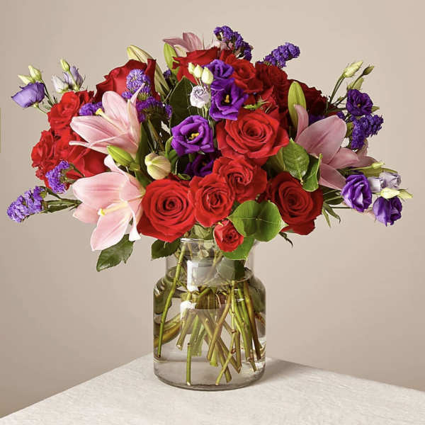 Bouquet of red roses, pink lilies, and purple flowers in a glass vase