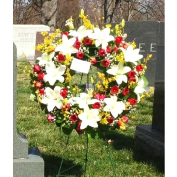 Standing wreath of white lilies, red roses, and yellow flowers on an easel in a cemetery.