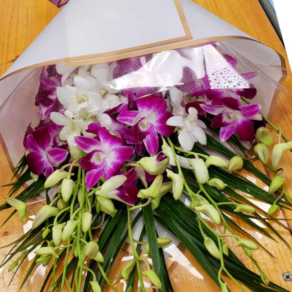 Wrapped bouquet of purple and white orchids with long green blades and a purple bow