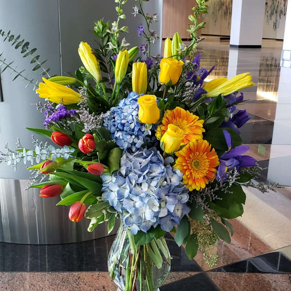 Colorful mixed bouquet in a clear glass vase with tulips, roses, hydrangeas, and gerbera daisies