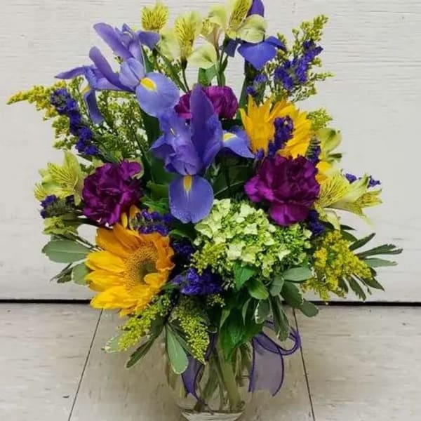 Mixed bouquet with purple, yellow, and blue flowers in a glass vase