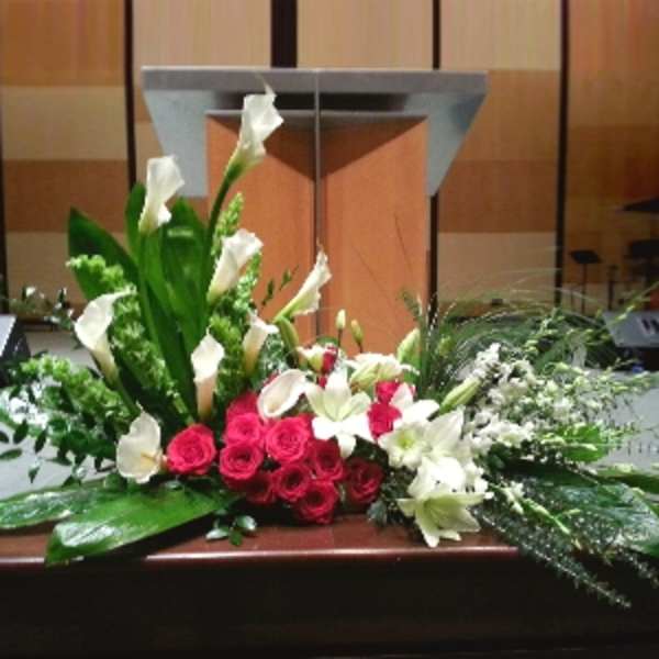 Large red and white floral spray with calla lilies, roses, and lilies arranged in front of a podium