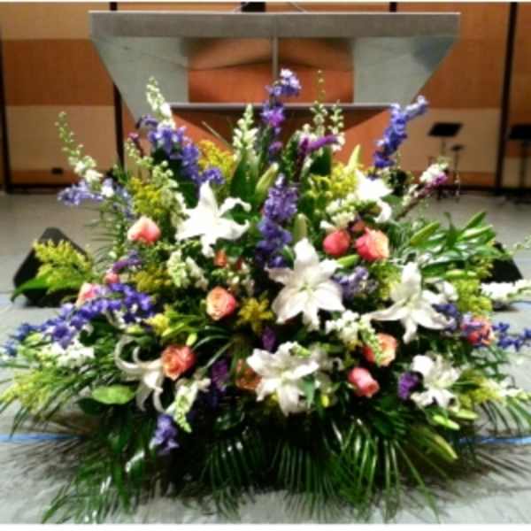 Large altar arrangement with white lilies, peach roses, and purple flowers on a stage