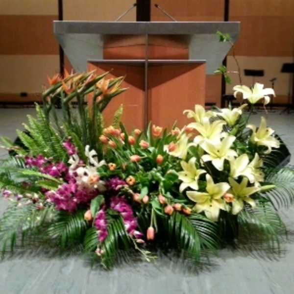 Large mixed floral arrangement with yellow lilies, orange tulips, and purple flowers in front of a podium