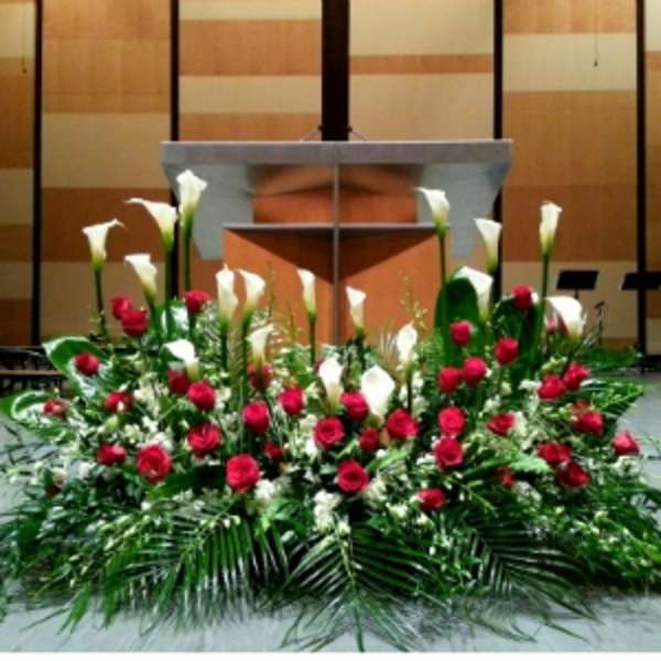 Large altar arrangement of red roses and white calla lilies in front of a church pulpit
