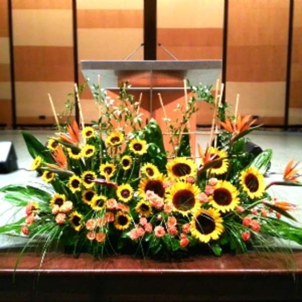 Large stage arrangement of yellow sunflowers and orange blooms in a low spray in front of a podium