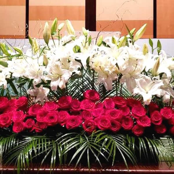 Large stage arrangement of red roses and white lilies with palm fronds in a long, low display