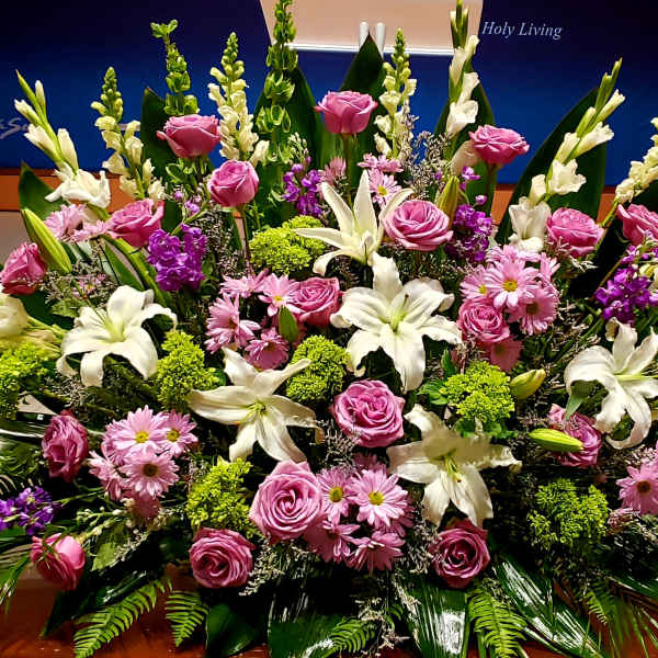 Large altar arrangement of white lilies, pink roses, and pink daisies with green and purple accents.
