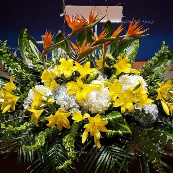 Large altar-style arrangement with yellow lilies, white hydrangeas, and orange tropical flowers in lush foliage