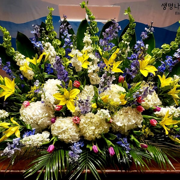 Large altar arrangement of yellow lilies, white hydrangeas and blue flowers in a fan-shaped display
