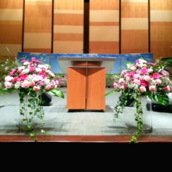 Two pink and white floral arrangements flank a podium on a stage