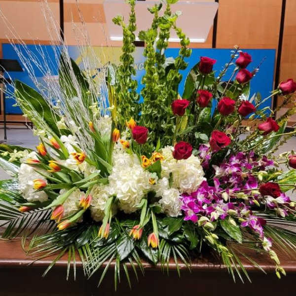Large mixed floral spray with red roses, white hydrangeas, yellow-red tulips, and purple orchids.