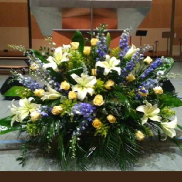 Large altar arrangement with white lilies, yellow roses, and purple flowers in a fan-shaped design