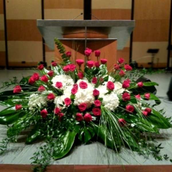 Large red rose and white flower spray with abundant foliage arranged in front of a podium