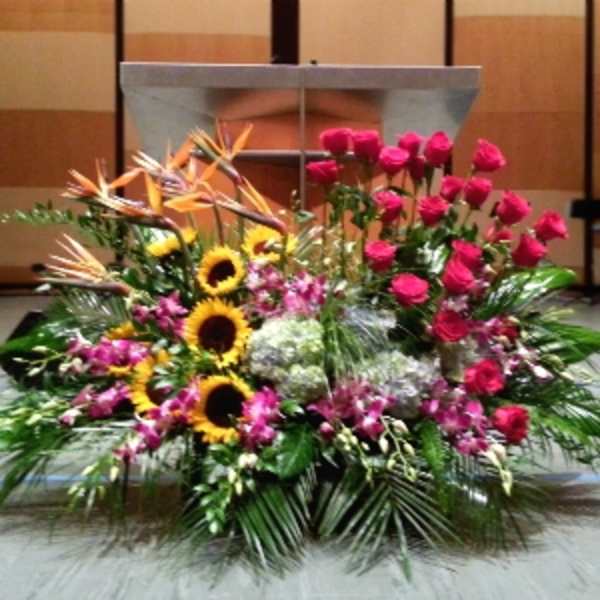 Large altar arrangement with pink roses, sunflowers, birds of paradise, orchids, and hydrangeas in a fan shape
