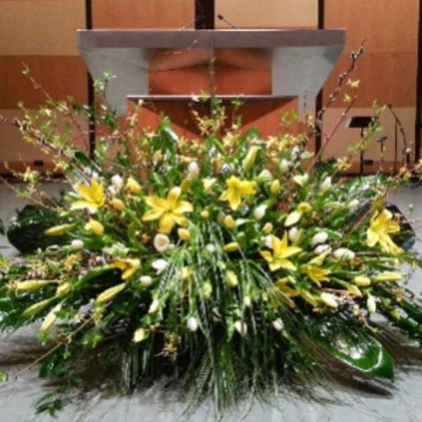 Large low yellow and white lily arrangement with abundant greenery in front of a podium