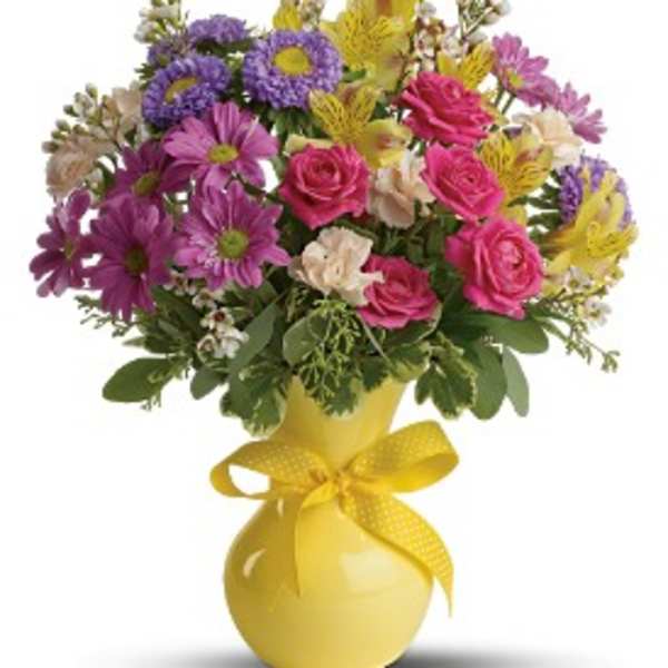 Mixed bouquet of pink, purple, and yellow flowers in a yellow vase with a ribbon
