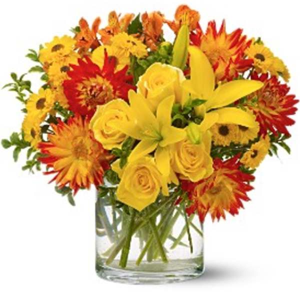 Yellow roses and lilies in a clear glass vase with red and orange daisies