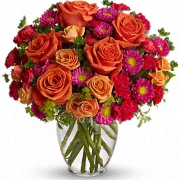 Bouquet of orange roses and magenta daisies in a clear glass vase
