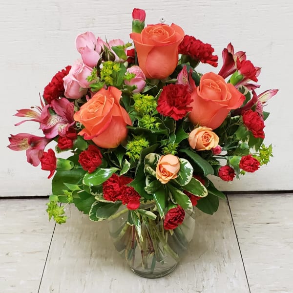 Bouquet of orange roses, red carnations, and pink alstroemeria in a glass vase