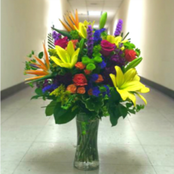 Tall mixed bouquet in a clear glass vase with bright lilies and roses
