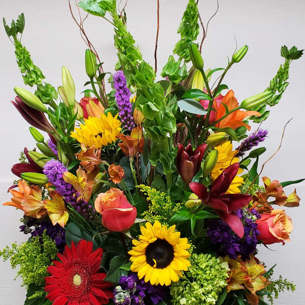 Tall mixed arrangement with sunflowers, lilies, roses, gerbera and bells of Ireland in a clear glass vase