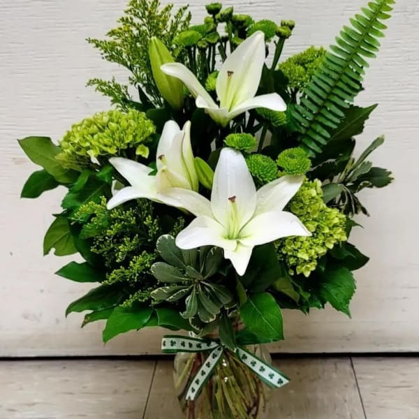 White lilies and green flowers arranged in a glass vase