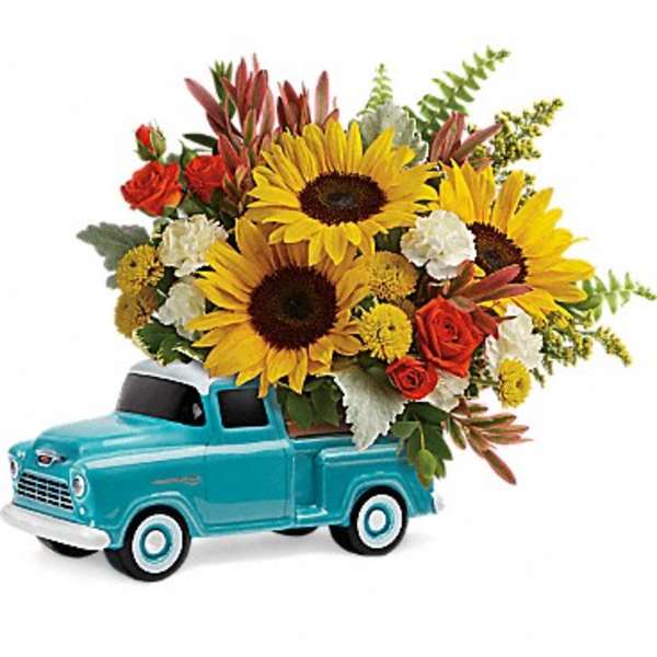 Bright sunflowers and mixed blooms arranged in a turquoise ceramic pickup truck container