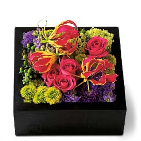 Square black box filled with hot pink roses, yellow-red tropical blooms, and green button flowers.