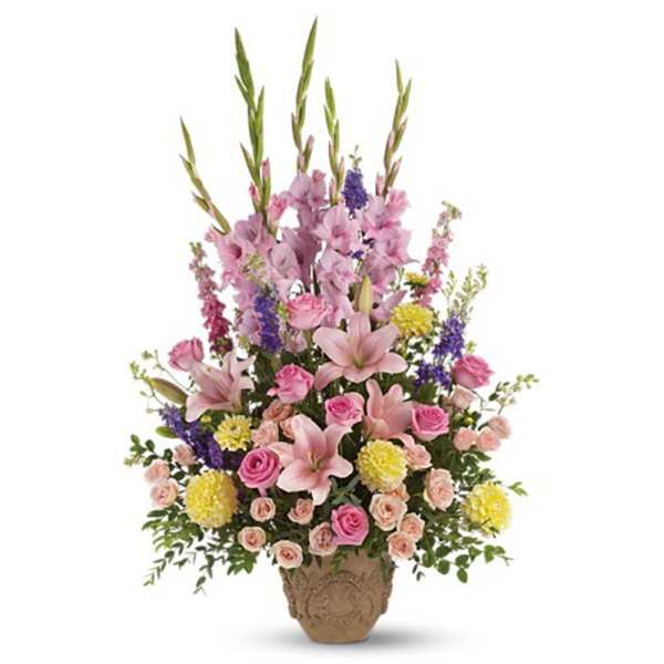 Tall arrangement of pink lilies and roses with yellow mums and purple flowers in a tan urn vase