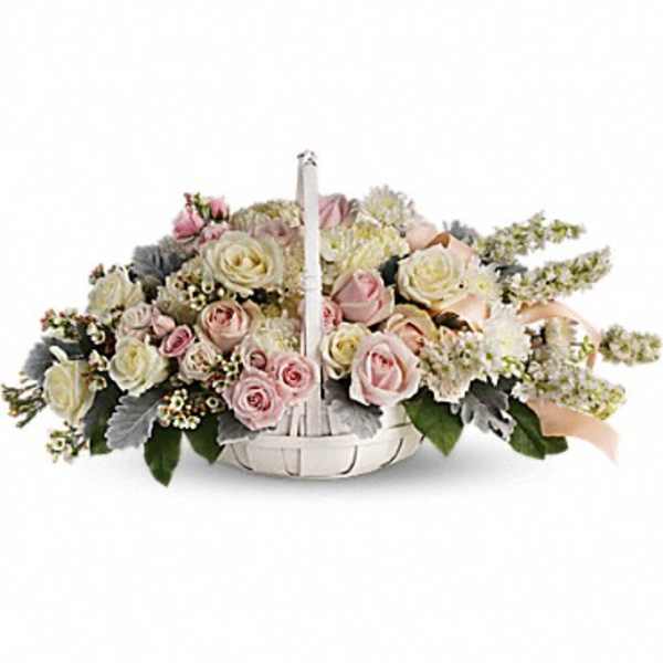 Low white basket arrangement of pale pink and ivory roses with soft fillers.