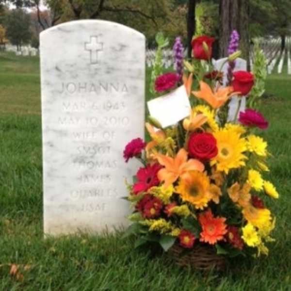 Colorful basket of yellow, orange, and red flowers placed beside a white cemetery headstone