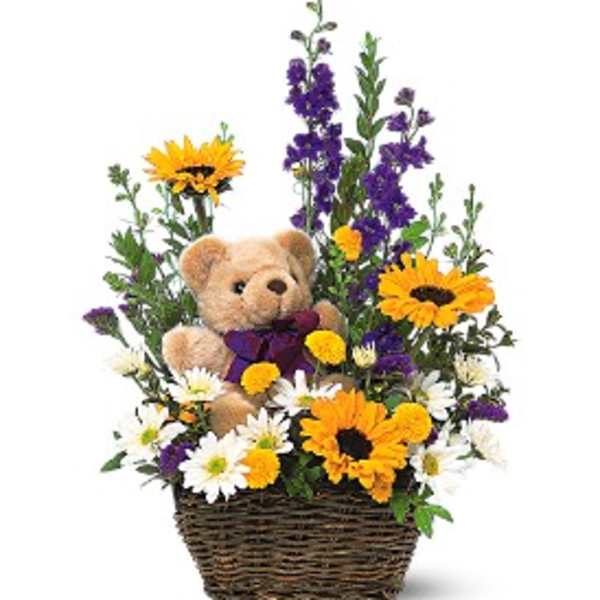 Basket arrangement with a teddy bear surrounded by yellow sunflowers, white daisies, and purple flowers