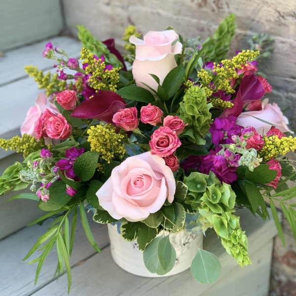 Pink roses and magenta flowers arranged in a white container