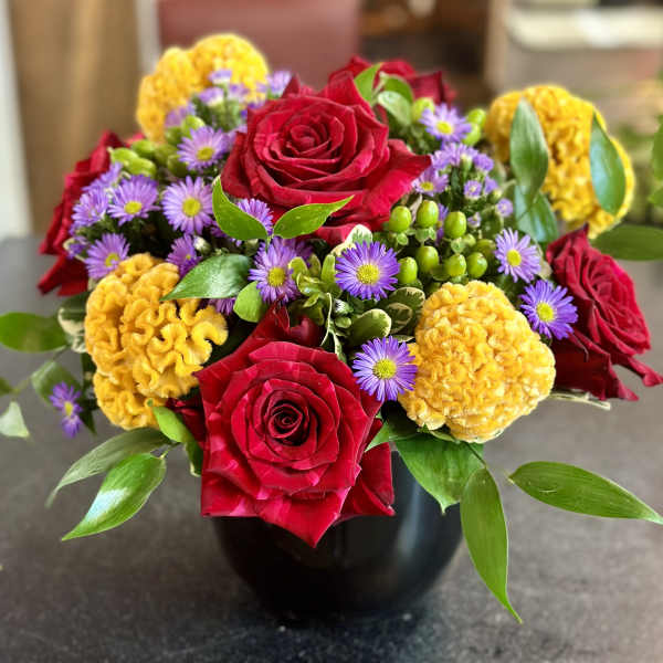 Bouquet of red roses, purple daisies, and yellow blooms in a black vase