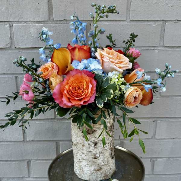Colorful bouquet with roses, calla lilies, and blue flowers in a birch vase